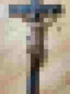 Restaurierte Jesusfigur auf Kruzifix mit Schäden und Holzmaserung auf hellem Untergrund.